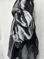 A close-up side view of a person wearing the Women Metallic Organza Black Pleated Dress, featuring shiny black voluminous puff sleeves with gathered elbow detail, set against a plain white background.