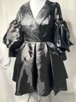 The Women Metallic Organza Black Pleated Dress features a shiny black finish, deep V-neckline, wide lapels, puffed long sleeves, and a flared pleated knee-length skirt, displayed on a white mannequin against a plain background.