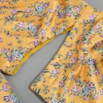 Close-up of the Hollowed-Out Hip Irregular Ruffled Floral Dress, featuring yellow satin fabric with purple, white, and blue floral print and long sleeves, displayed flat on a neutral background.