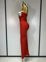 A gold mannequin showcases the Crystal Bust Long Bodycon Dress—a fitted, strapless red gown with a side slit, pearl detailing around the bust, and a smooth silhouette—set against a plain backdrop with light-colored panels.
