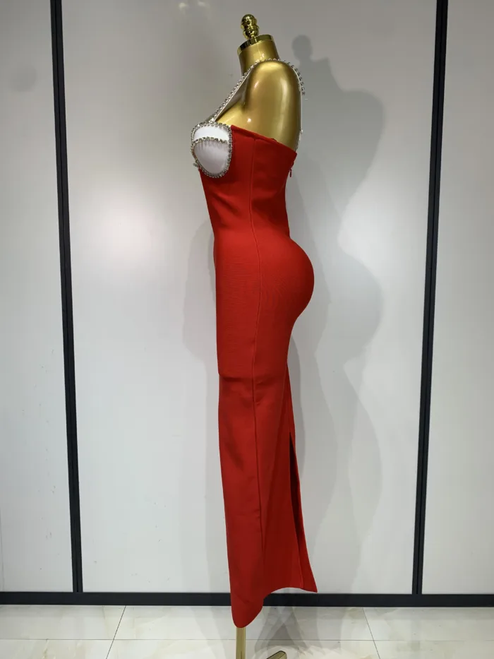 A gold mannequin showcases the Crystal Bust Long Bodycon Dress—a fitted, strapless red gown with a side slit, pearl detailing around the bust, and a smooth silhouette—set against a plain backdrop with light-colored panels.