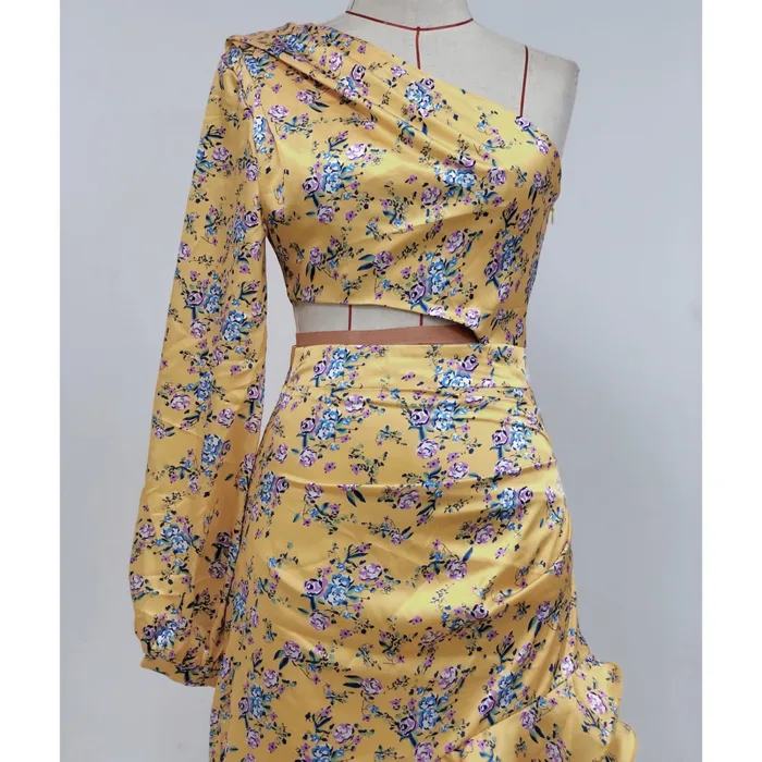 A mannequin showcases the Hollowed-Out Hip Irregular Ruffled Floral Dress: a yellow, one-shoulder design with a single long sleeve, fitted waist, and blue and purple floral patterns with green leaves.
