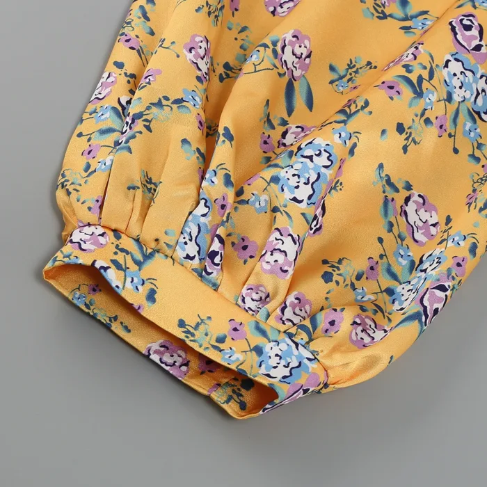 Close-up of the yellow Hollowed-Out Hip Irregular Ruffled Floral Dress, featuring a purple, blue, and white floral print, with an elastic cuff on its long sleeve against a gray background.