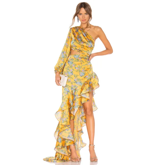 A woman wears the Hollowed-Out Hip Irregular Ruffled Floral Dress, a yellow floral one-shoulder style with ruffles and an asymmetrical hem. She accessorizes with a white clutch and nude heels, posing against a white background.