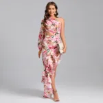 A woman models the Hollowed-Out Hip Irregular Ruffled Floral Dress, featuring florals, ruffles, and a side cutout. She poses against a gray background, holding a beige clutch and wearing strappy heels with a bright smile.