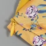 A close-up of the Hollowed-Out Hip Irregular Ruffled Floral Dress, featuring a floral pattern with pink, purple, and blue flowers and green leaves on yellow fabric, shown against a smooth gray background.