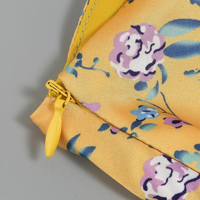 A close-up of the Hollowed-Out Hip Irregular Ruffled Floral Dress, featuring a floral pattern with pink, purple, and blue flowers and green leaves on yellow fabric, shown against a smooth gray background.