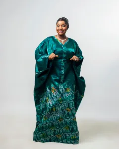 A person wearing a flowing green traditional dress made of liquid Mikado fabric, featuring wide sleeves and intricate multicolored African print embroidery. The outfit blends cultural richness with modern elegance, standing out against a plain background.