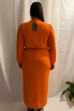 A plus-size model poses confidently in a vibrant orange chiffon and crepe dress with crystal embellishments, standing against a white backdrop.