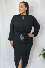 A plus-size model poses confidently in a vibrant black chiffon and crepe dress with crystal embellishments, standing against a white backdrop.