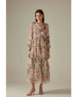 A woman wearing floral translucent patchwork dress with long sleeves, an O-neckline, ankle-length hem, and decorative ruffles, embroidery, and hollow-out details.
