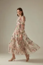 A woman wearing floral translucent patchwork dress with long sleeves, an O-neckline, ankle-length hem, and decorative ruffles, embroidery, and hollow-out details.