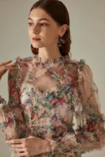 A woman wearing floral translucent patchwork dress with long sleeves, an O-neckline, ankle-length hem, and decorative ruffles, embroidery, and hollow-out details.