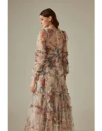 A woman wearing floral translucent patchwork dress with long sleeves, an O-neckline, ankle-length hem, and decorative ruffles, embroidery, and hollow-out details.